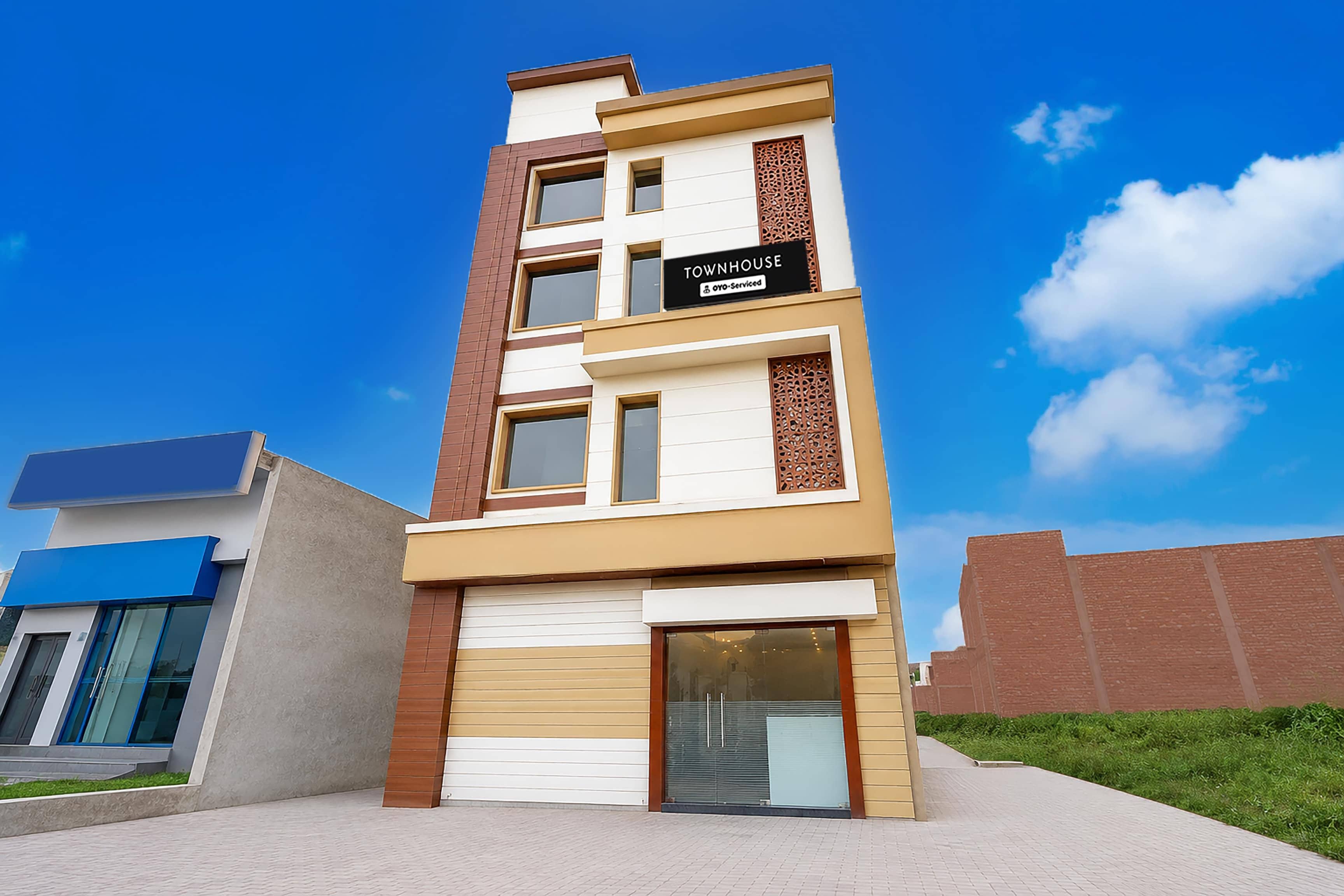 A modern townhouse with a flat roof, large windows, and a sign indicating it is serviced by Oyo.