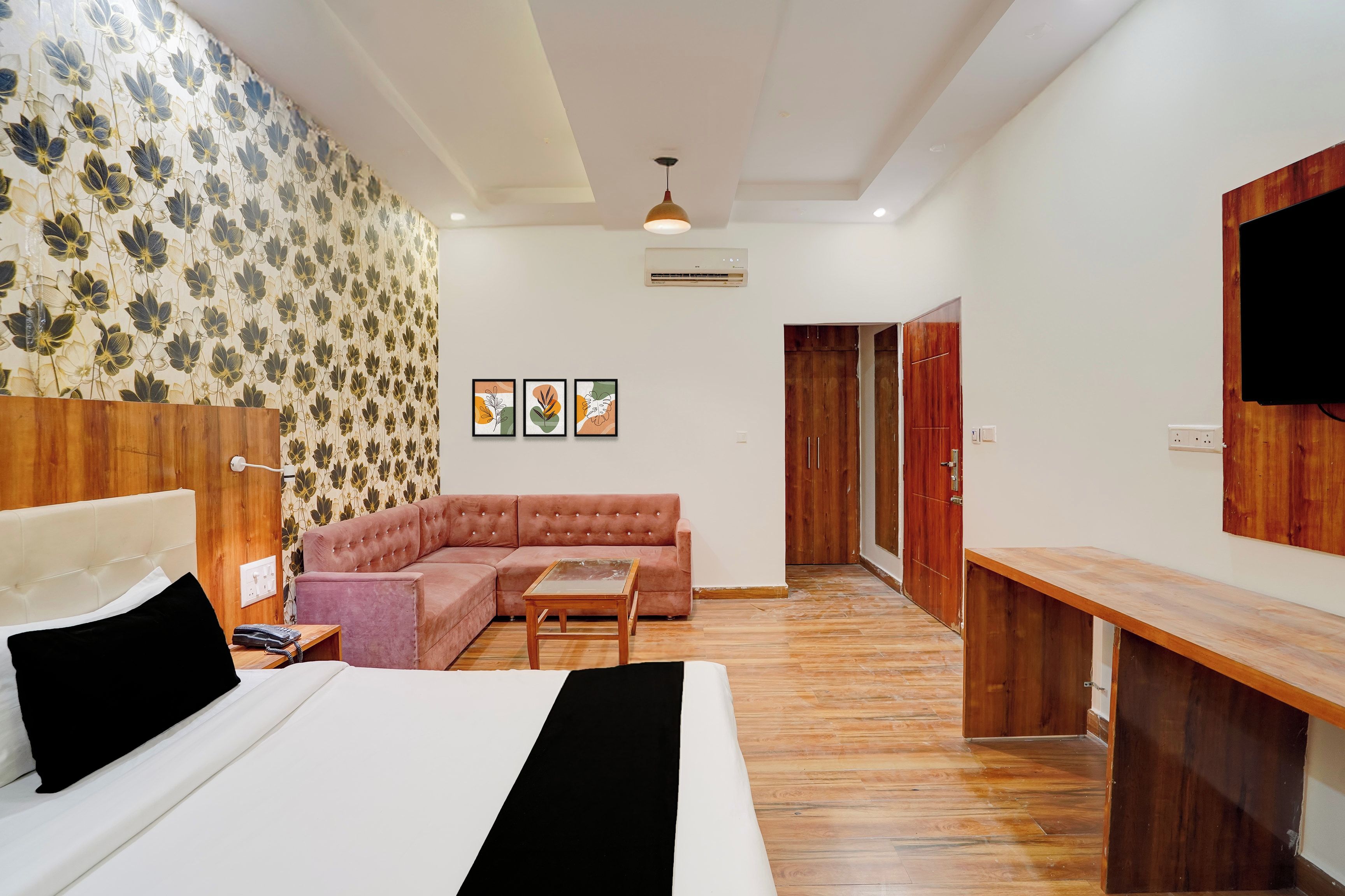 Une chambre moderne avec un lit, un canapé, une table de chevet en bois et un téléviseur fixé au mur.