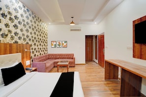 A modern bedroom with a bed, a sofa, a wooden nightstand, and a TV mounted on the wall.