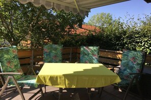 An outdoor patio with a table and chairs, surrounded by a wooden fence and greenery. - in the Vogler House Apartment (Bad Hindelang)