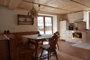 Een eetruimte met een houten tafel en stoelen, een hanglamp en een keuken met witte kastjes en een fornuis.