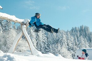 Una persona haciendo snowboard sobre un riel en un bosque nevado.