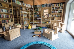 A room with wooden bookshelves filled with books, a wooden desk, a blue trampoline, and various toys. - Organic farm with 2 bedrooms (Missen-Wilhams)