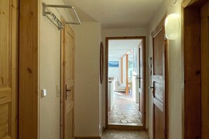 A hallway with wooden doors, a hanging towel rack, and a view into a room with a stone floor. - Holiday apartment with 1 bedroom (Lindau)