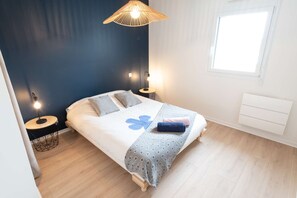 A bedroom with a bed, bedside lamps, a window, and a radiator. - Elegant 2-bedroom beachfront apartment by Groom* (Ploemeur)