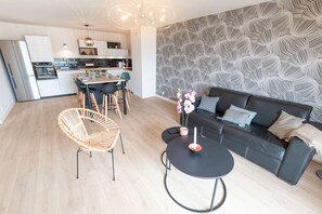 A modern living space with a dining area, a black sofa, a round coffee table, and a wicker chair. - Elegant 2-bedroom beachfront apartment by Groom* (Ploemeur)