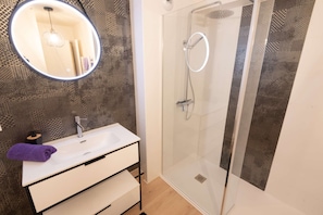 A modern bathroom with a glass shower enclosure, a white sink with a mirror, and a patterned wall. - Elegant 2-bedroom beachfront apartment by Groom* (Ploemeur)