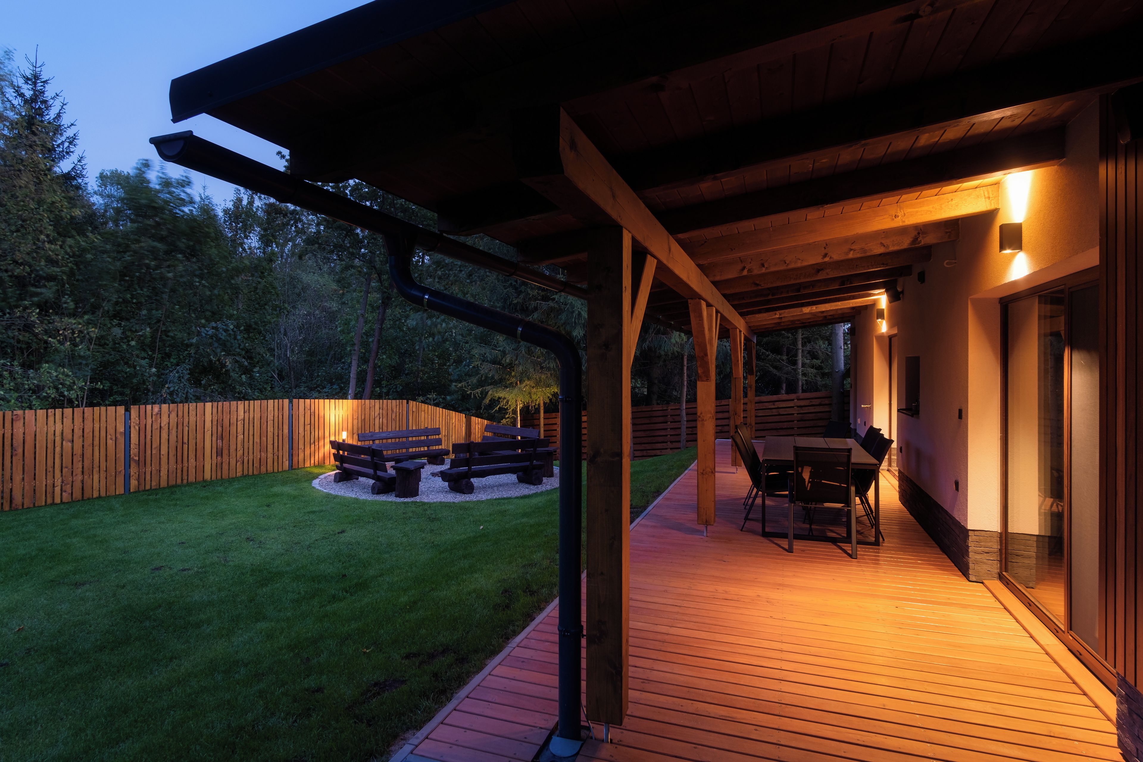 An outdoor deck with a wooden floor, a covered seating area with benches, and a table with chairs.