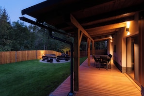 Una terraza exterior con piso de madera, un área de estar cubierta con bancos y una mesa con sillas.