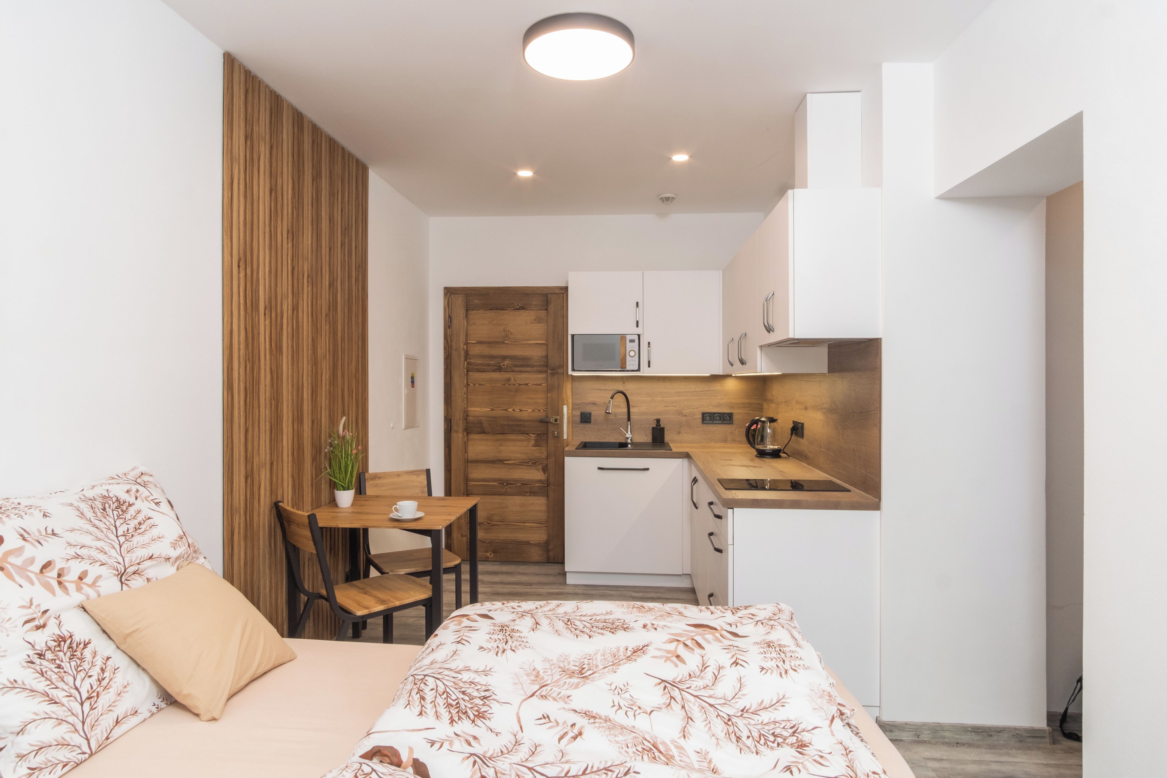A compact room with a bed, a small dining table, and a kitchenette.