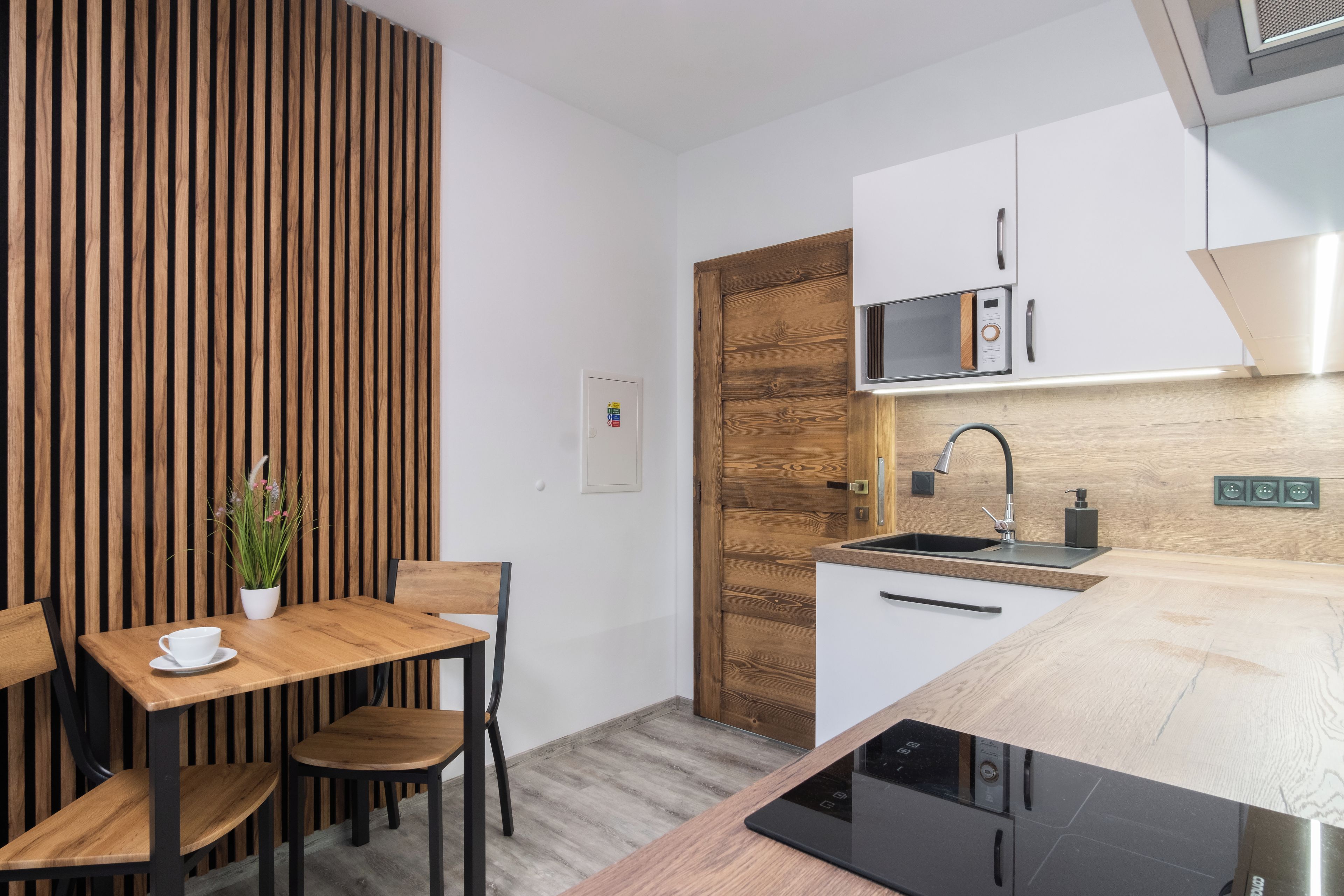 Cozinha moderna com parede em madeira, área de refeições com mesa e cadeiras, e micro-ondas embutido.