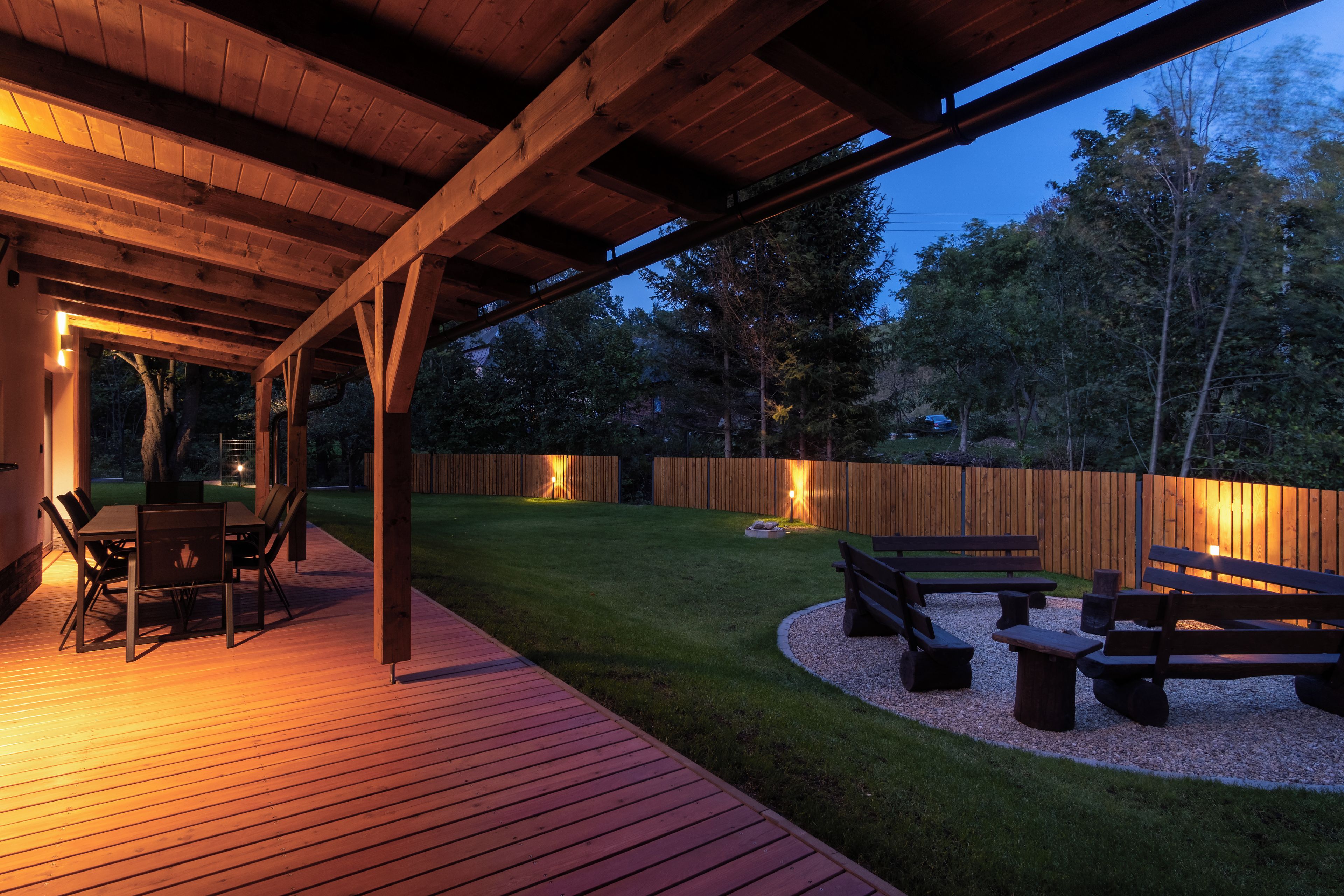 An outdoor patio with a wooden deck, a table with chairs, and a fire pit area.