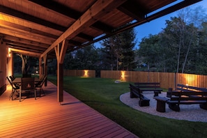 Un patio exterior con terraza de madera, una mesa con sillas y una zona con pozo de fuego.