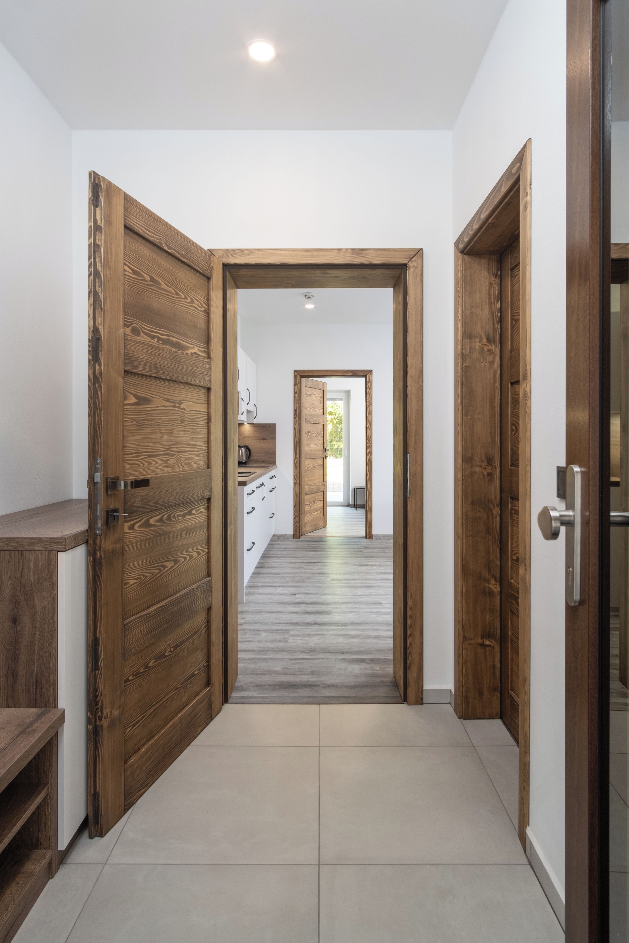 A hallway with wooden doors and a kitchen area visible through an open door.