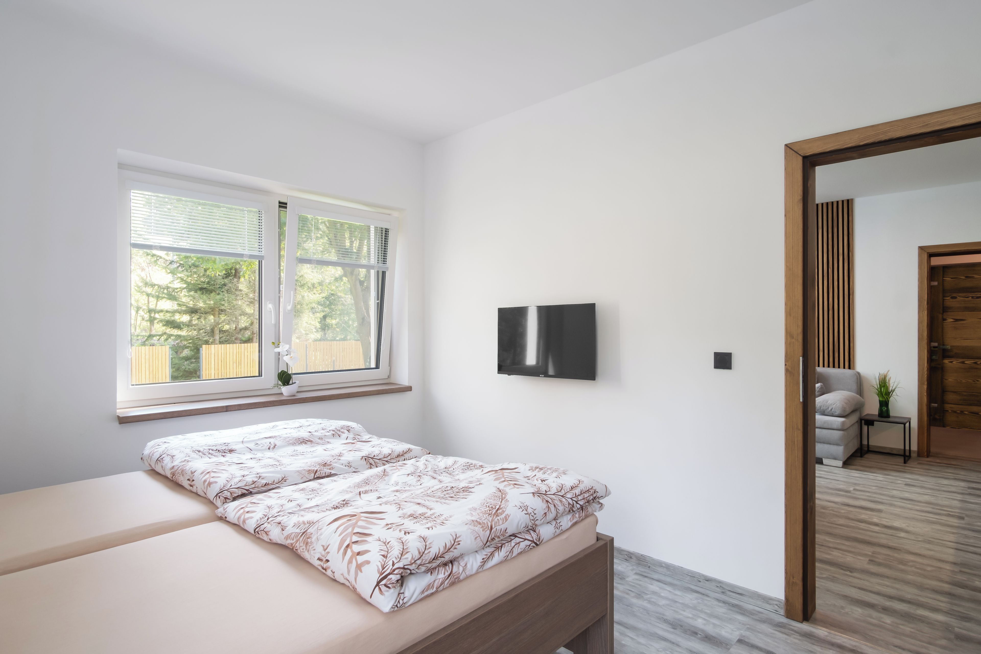 A bedroom with a bed, a window with blinds, a flat-screen TV, and a wooden door.