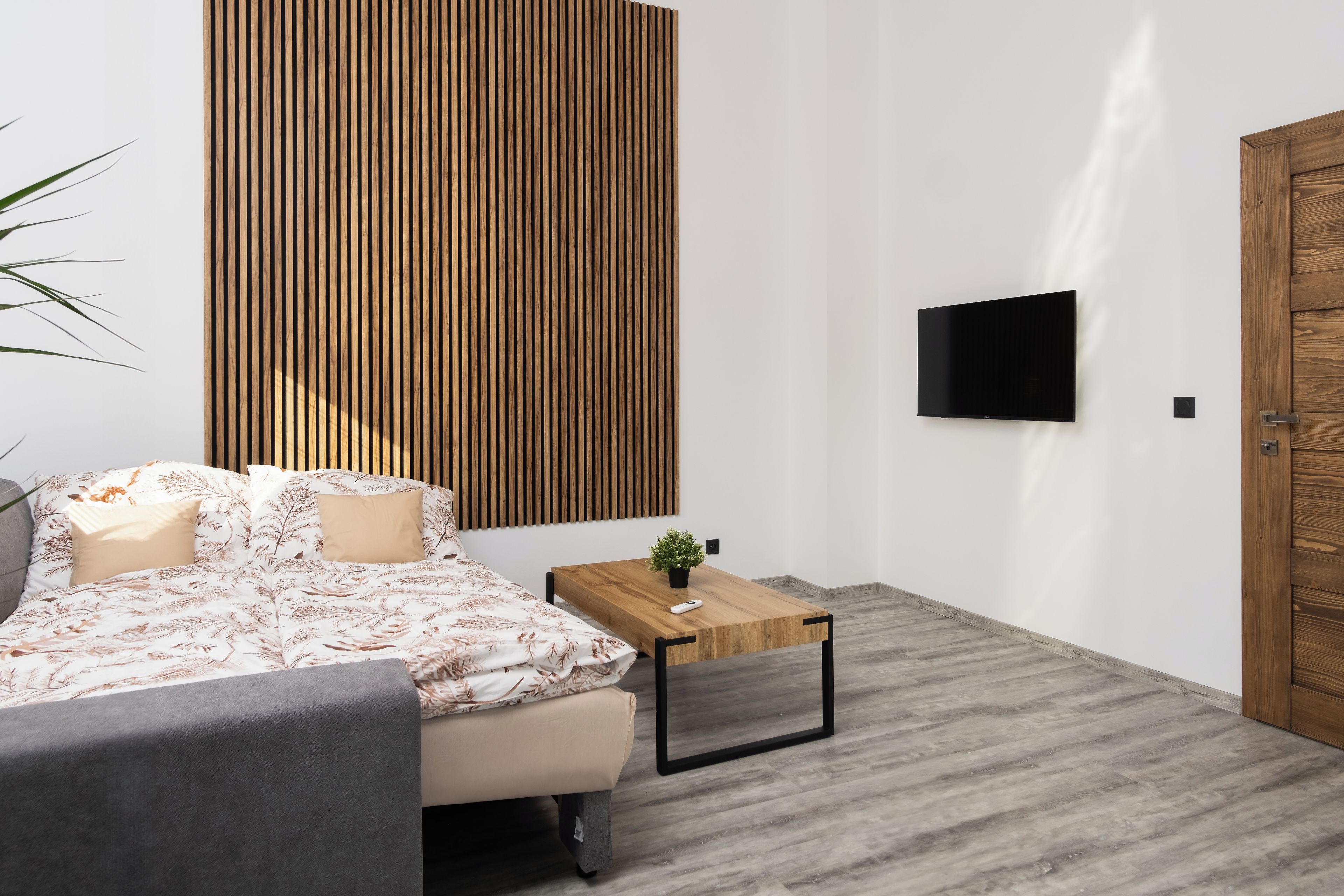 A modern bedroom with a bed, a wooden panel wall, a TV, and a wooden door.