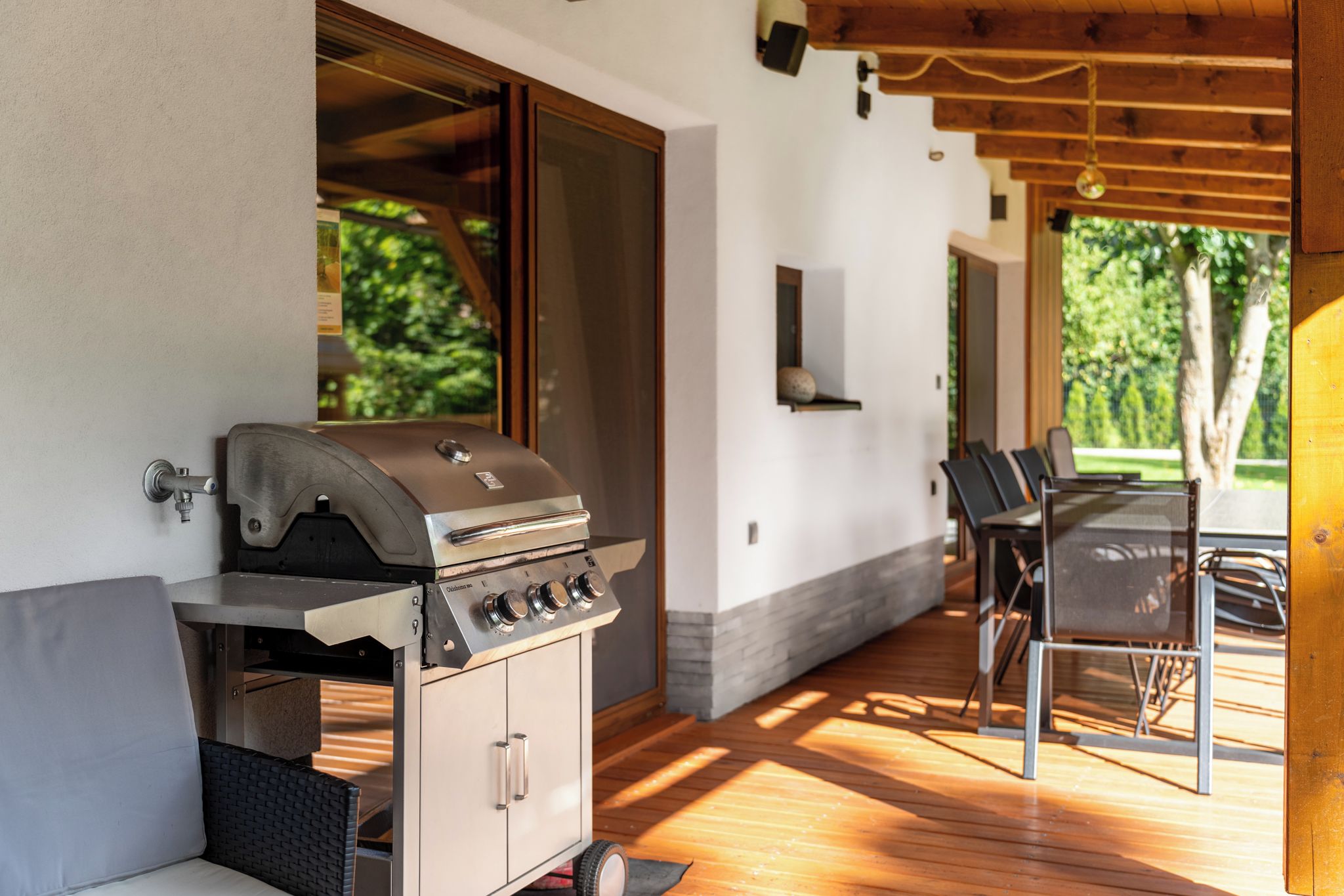 An outdoor patio with a barbecue grill, seating area, and a view of greenery.