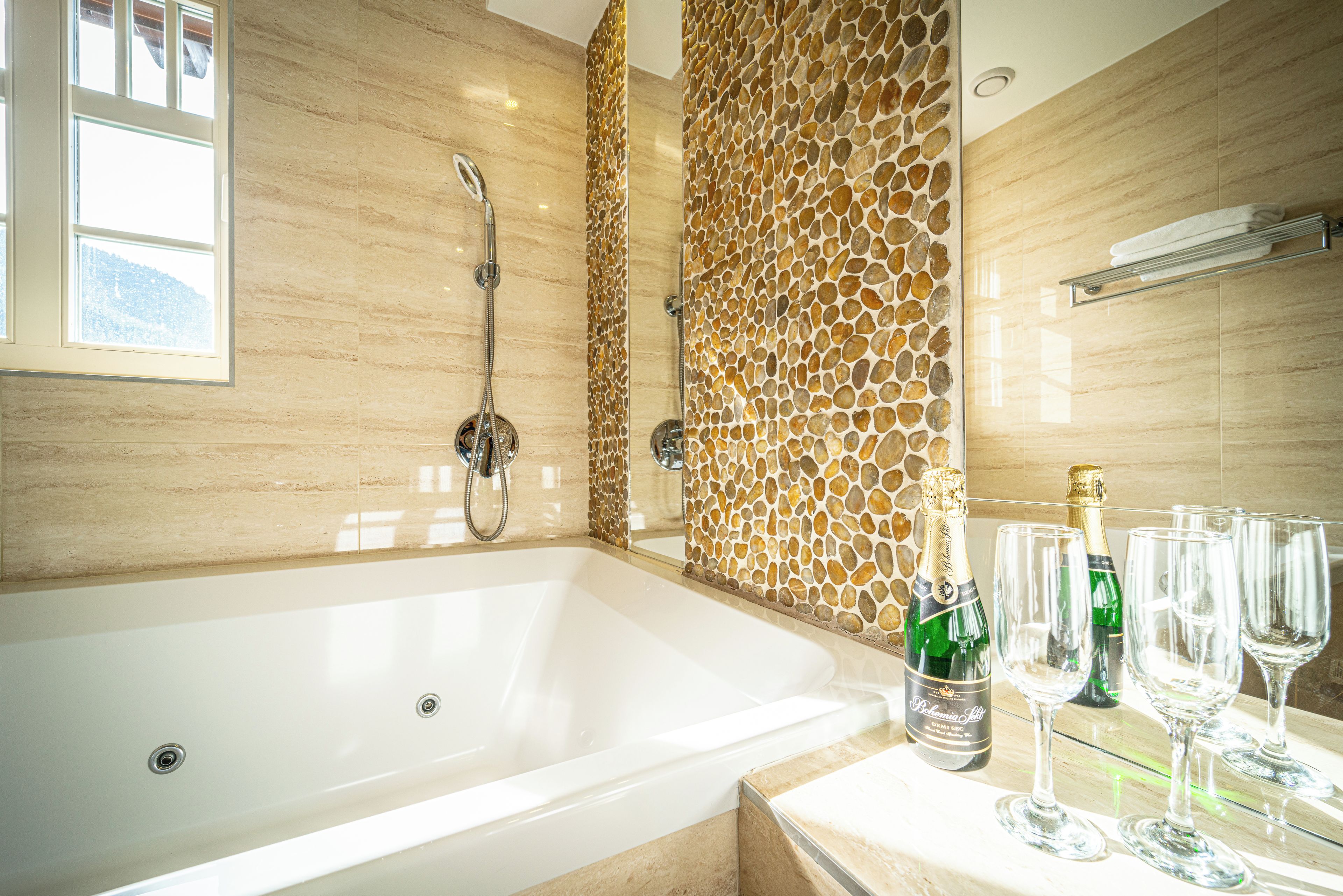 A modern bathroom with a large bathtub, a shower, and a decorative stone wall.