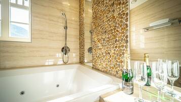 A modern bathroom with a large bathtub, a shower, and a decorative stone wall.