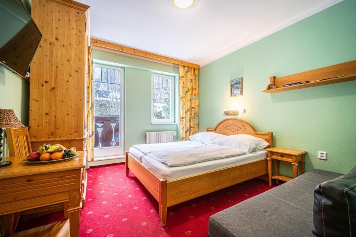 A bedroom with a wooden bed, a desk with fruit, a red carpet, and a view through a glass door.