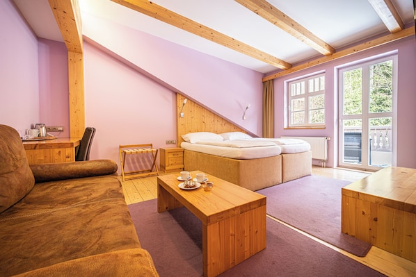 A cozy room with a wooden ceiling, a sofa, a small table with a tray, a bed with a headboard, and a window with curtains.