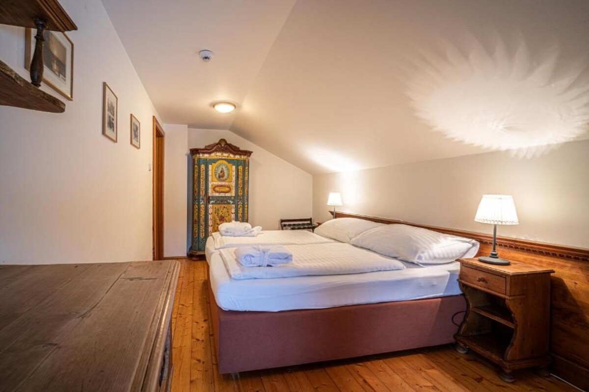 A hotel room with a wooden floor, a bed with white linens, a nightstand, a lamp, and a decorative ceiling.