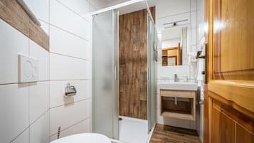Un baño moderno con cabina de ducha de vidrio, un inodoro blanco y un mueble de tocador de madera.
