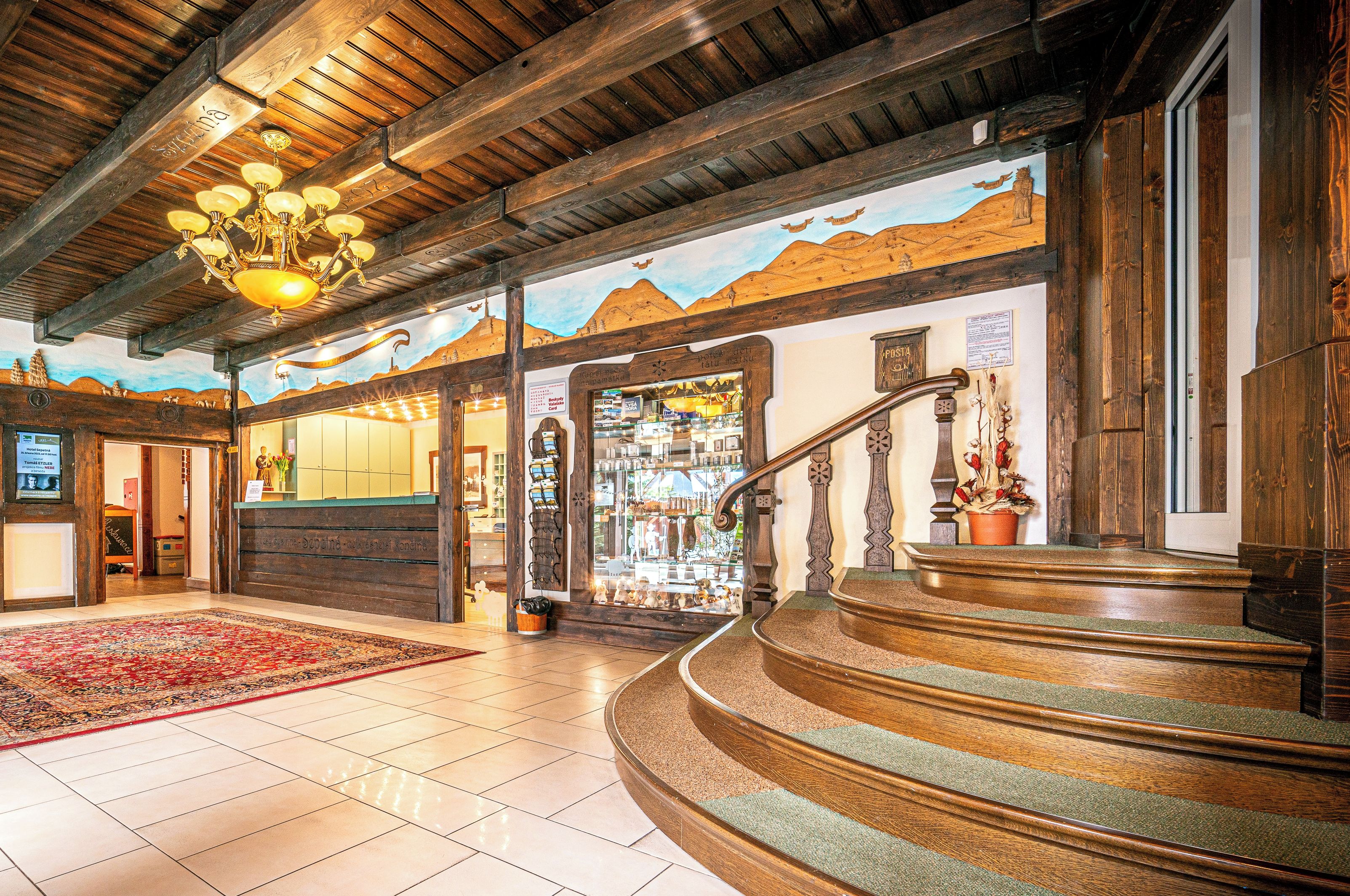 A hotel lobby with a wooden staircase, a reception desk, and a mountain-themed mural on the wall.