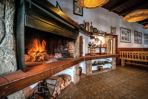 Un interior rústico con chimenea de piedra, estantes de madera con diversos objetos y un banco.