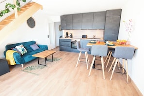 A compact living space with a kitchenette, a sofa, a dining table, and a staircase. - Duplex with Balcony, Sea and Beach View, by Groom* (Ploemeur)