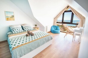 Ein Schlafzimmer mit einem Bett, einem Sessel, Meerblick und einem Vorhangfenster.