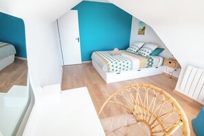 A bedroom with a sloped ceiling, a bed with patterned bedding, a wicker chair, and a white bedside table. - Duplex with Balcony, Sea and Beach View, by Groom* (Ploemeur)