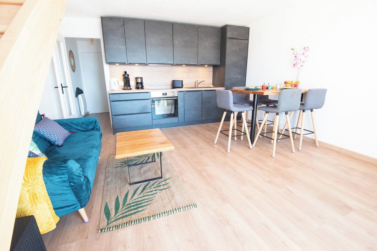 A compact living space with a kitchenette, a dining area with a table and chairs, and a sofa with a patterned throw.