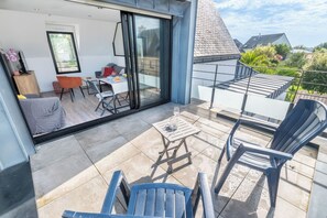 A modern balcony with a glass door leading to a dining area, outdoor seating, and a view of the neighborhood. - Beautiful house between Ocean and Countryside by Groom* (Guidel)
