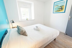 A neatly made bed with a pillow and a rolled towel, a window with a view, and a framed picture on the wall. - Beautiful house between Ocean and Countryside by Groom* (Guidel)