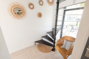 En modern inredning med en spiraltrappa, en fåtölj i rotting och dekorativ väggkonst.