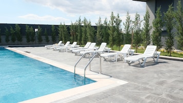 Una piscina con sillas reclinables blancas y una escalera metálica.
