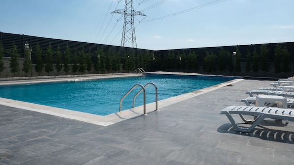 A swimming pool with a metal ladder, surrounded by a tiled deck and white lounge chairs.