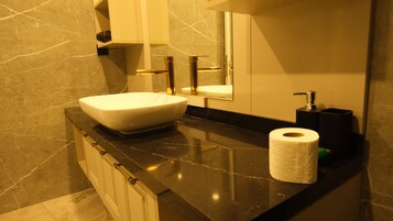 Un baño con encimera de mármol, un lavamanos blanco, un espejo, un dispensador de papel higiénico y un dispensador de toallas.