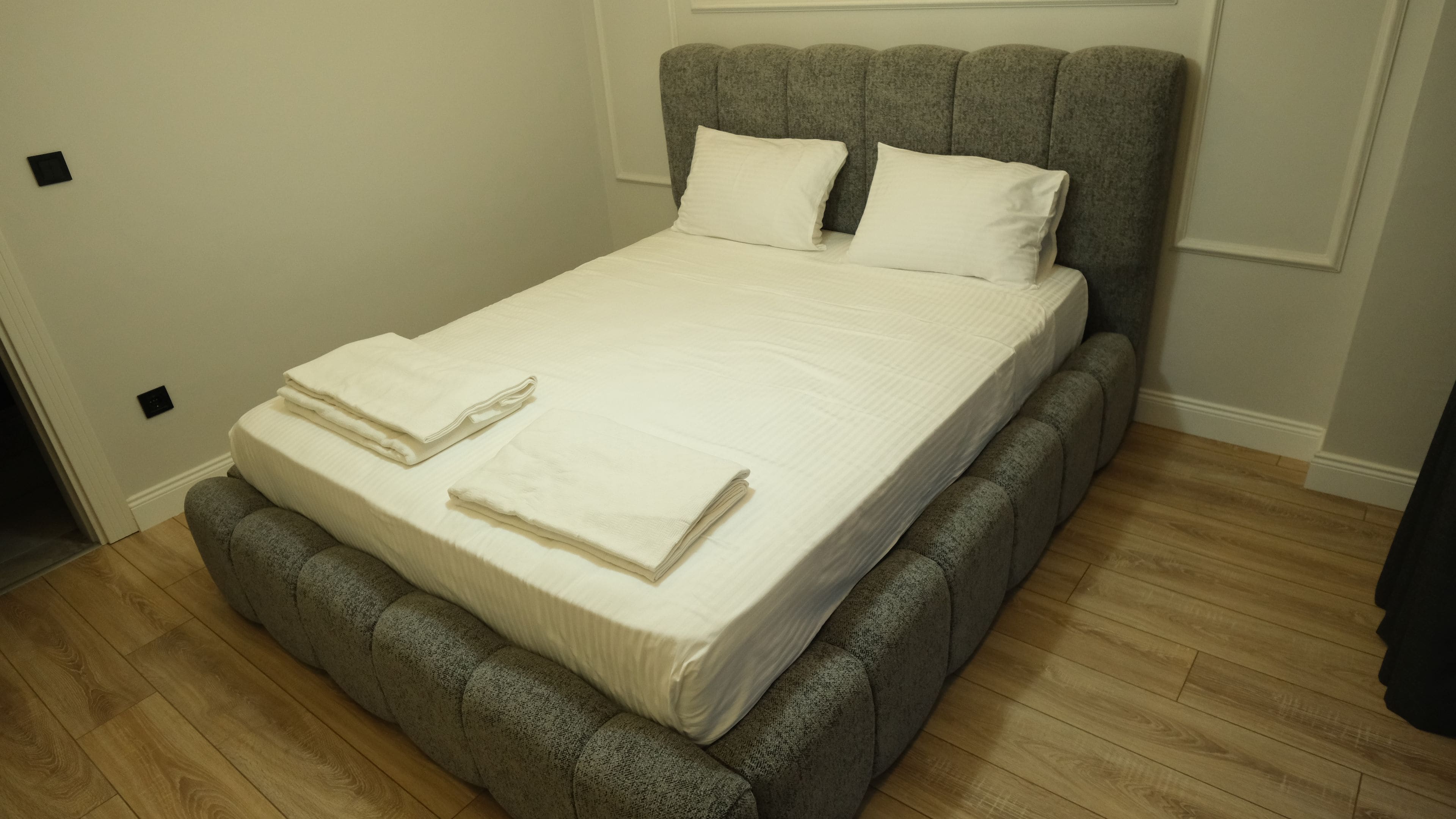 Una cama bien hecha con un cabecero tapizado en gris y un colchón blanco.