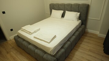 Una cama bien hecha con un cabecero tapizado en gris y un colchón blanco.
