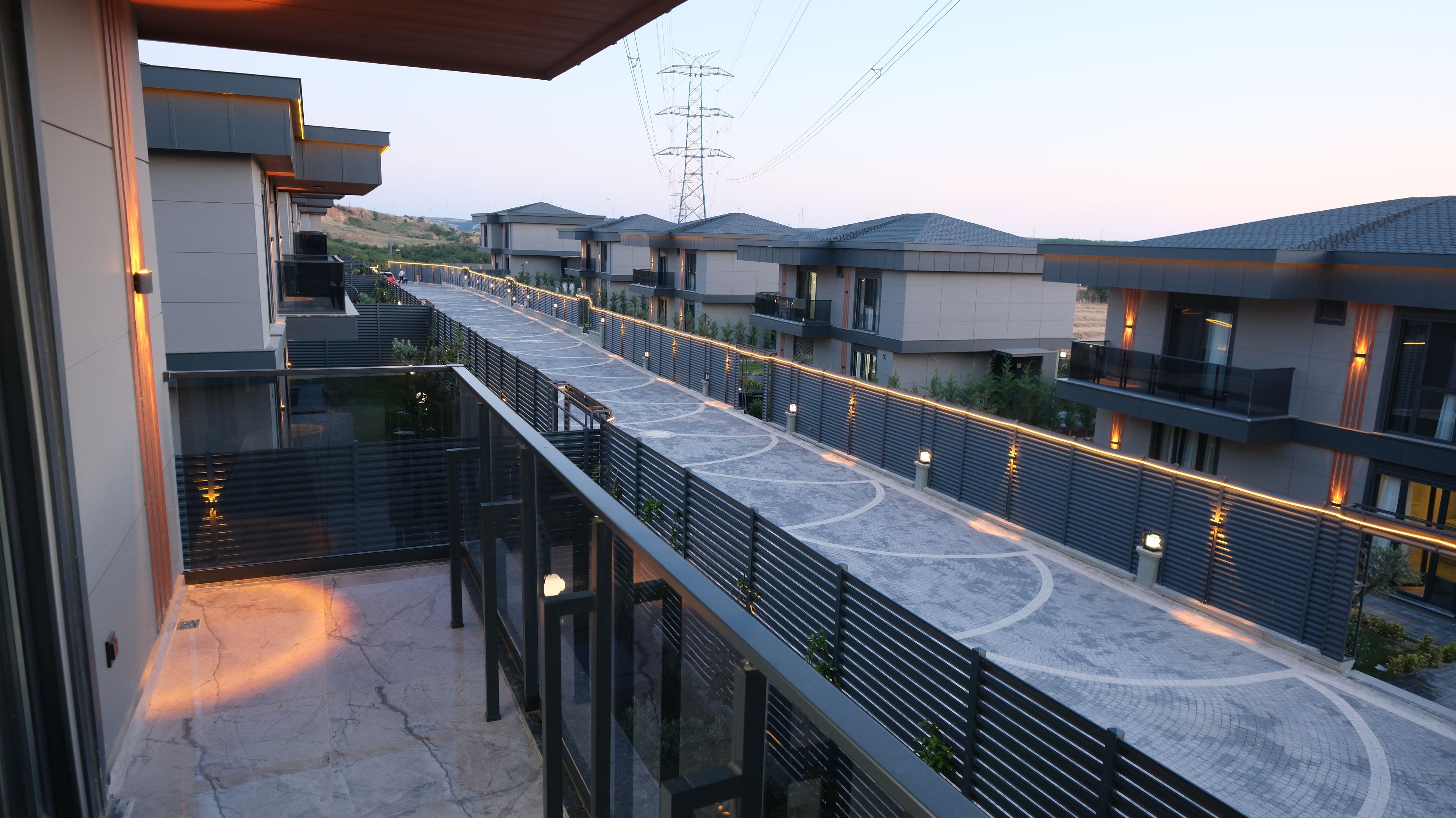 A modern residential area with a paved walkway, balconies, and a view of power lines.