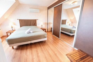 Quarto com cama, mesas de cabeceira, um espelho e um banco de madeira.