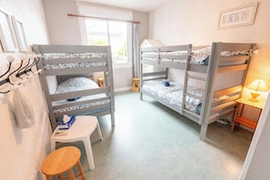 A room with bunk beds, a small stool, a table with a lamp, and a window with curtains. - Breton family home, within walking distance of the beach – by Groom* (Ploemeur)