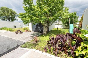 Ein wohnlicher Außenbereich mit Baum, Schaukel, Picknicktisch und kleinem Garten.