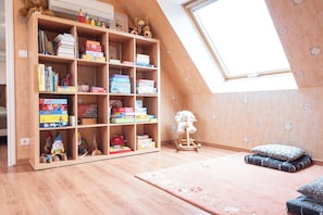 A room with a sloped ceiling, a wooden bookshelf filled with books and toys, a rocking horse, and a patterned rug. - Breton family home, within walking distance of the beach – by Groom* (Ploemeur)