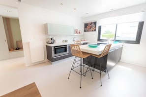 A modern kitchen with a dining area, featuring a white countertop, two chairs, and a window with a view. - Stunning Premium Villa, beaches within walking distance via Groom* (Larmor-Plage)