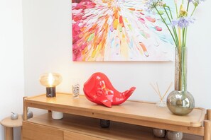 Una scrivania in legno con una scultura di balena rossa, un vaso di vetro con fiori e un quadro astratto appeso al muro.