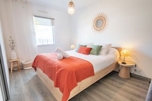 Une chambre à coucher avec un lit, des lampes de chevet, une fenêtre et un grand miroir rond fixé au mur.