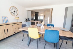 Moderni ruokailutila, jossa on puinen pöytä, neljä tuolia ja seinälle kiinnitetty kello.